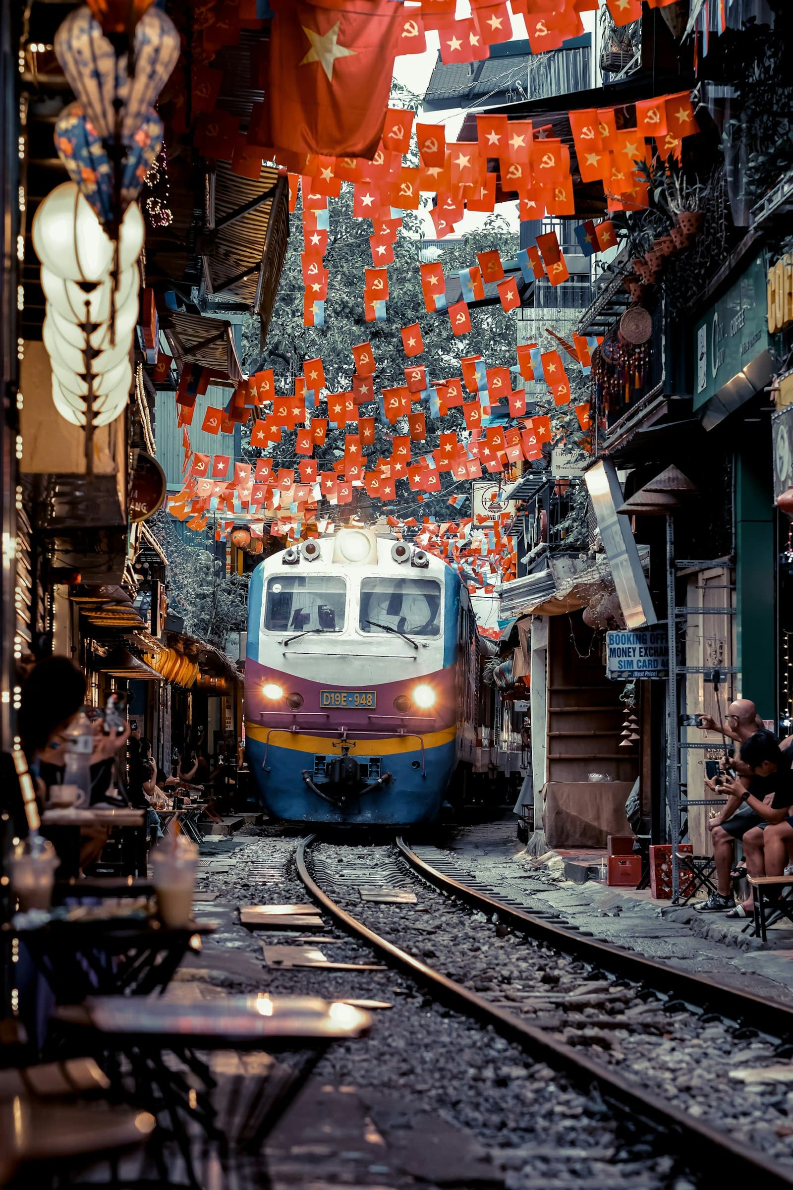 The Reunification Express easing through Hanoi's Train Street beneath strings of red flags