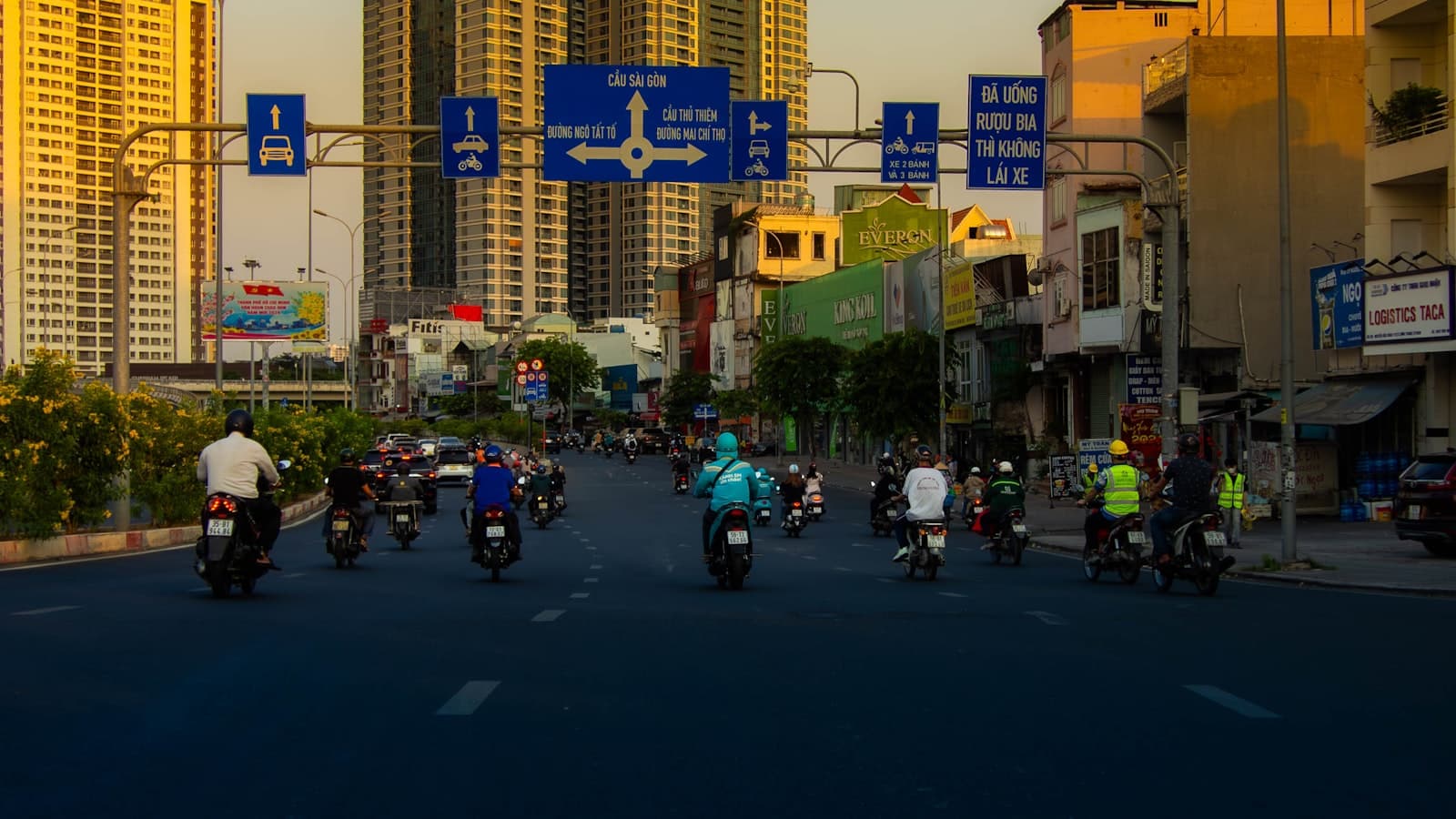 Motorbikes flowing down a wide Saigon boulevard at golden hour, towers rising behind